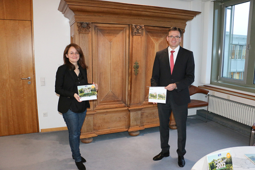 Das Bild zeigt die Leiterin der Stabsstelle Tourismus, Ricarda Grünig bei der Übergabe des Kalenders an Landrat Dr. Joachim Bläse.